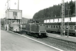 schwarz-weiß Fotografie von 1971. Es ist eine Lok im Bahnhofsbereich zu sehen. Auf den Schienen dahinter ist ebenfalls ein Zug mit mehreren Waggons zu sehen.