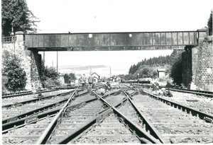 schwarz-weiß Aufnahme des ehemaligen Gleisdreiecks in Nonnweiler. Im Vordergrund sind die Schienenführungen zu sehen, sie führen teils parallel, verlaufen aber auch teilweise ineinander. Über die Gleise führt eine Brücke. Am linken und rechten Bildrand sind die Brückenpfeiler zu sehen.