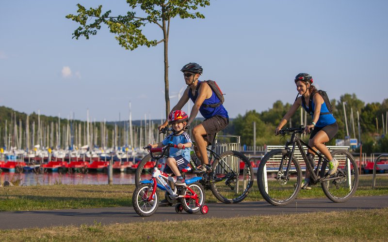 Eine Familie (Mann Frau und Kind) führt am Rande des Bostalsees Fahrrad