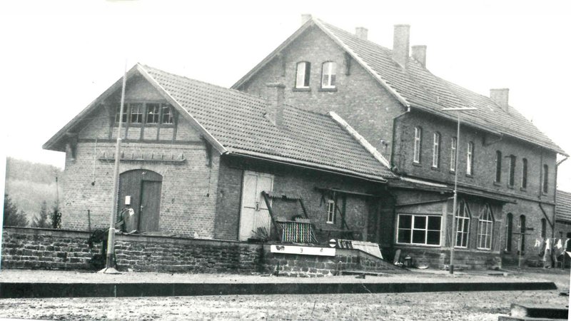 schwarz-weiß Aufnahme des Bahnhofgebäudes in Nonnweiler aus dem Jahr 1978. Es besteht aus 2 aneinander gebauten Häuschen, das linke ist etwas kleiner und niedriger, der rechte etwas höher und größer.