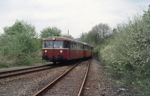 Museumszug der Hochwaldbahn auf der Strecke. Der rote Museumszug fährt auf den Gleisen, rechts und links von den Schienen sind Büsche und Bäume zu sehen